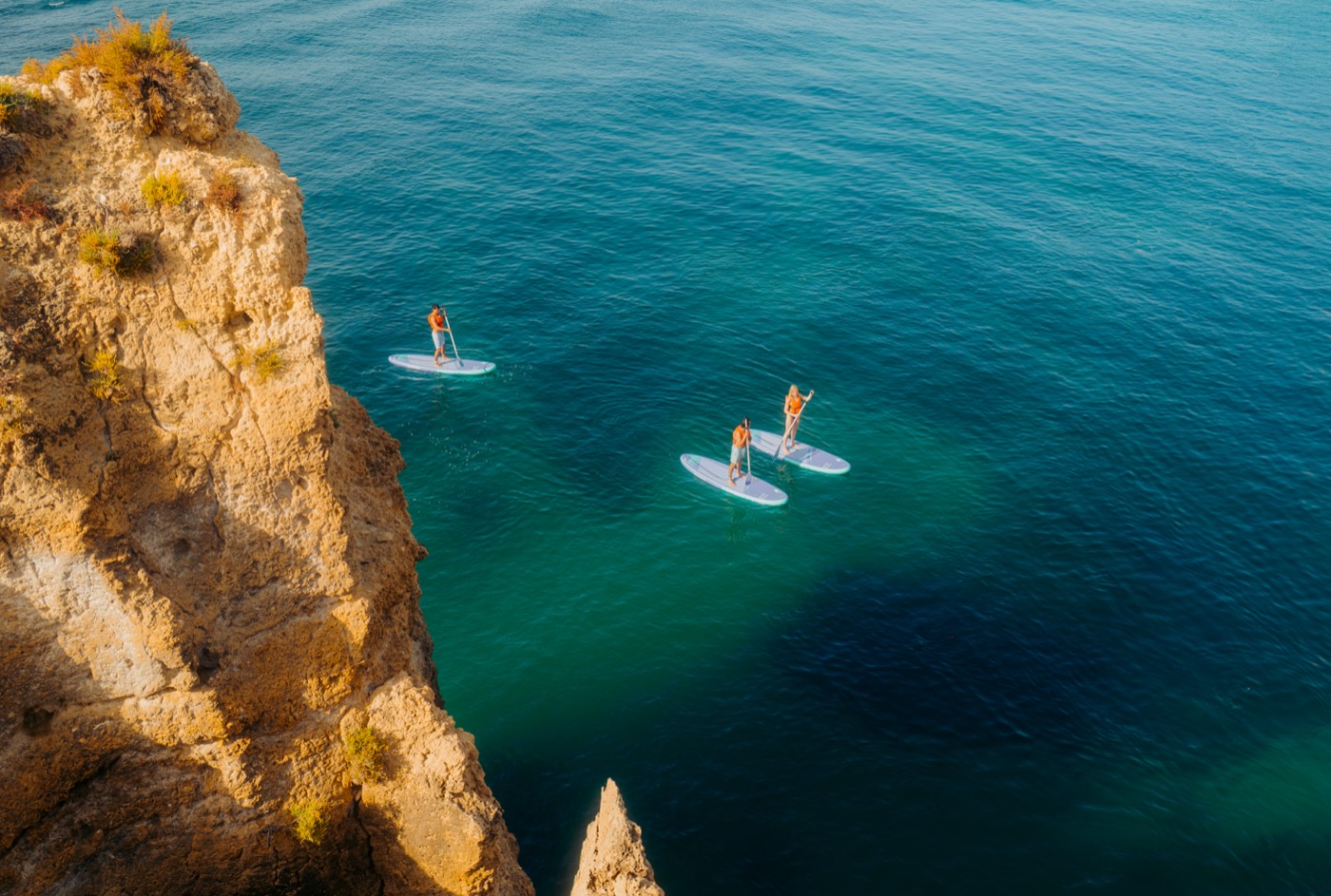 Aerial view of three paddlers beside Algarve cliffs