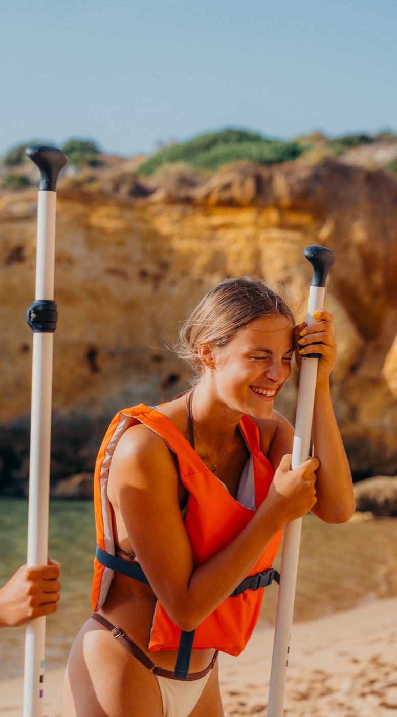 Paddler laughing with paddles at golden hour, Algarve cliffs